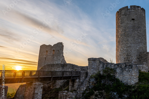 Burgruine Wolfstein mit Brücke, Burgfried und Mauerresten im Abendlicht mit Sonnenuntergang in gelb über der Brücke und leicht bewölktem blauen Abendhimmel