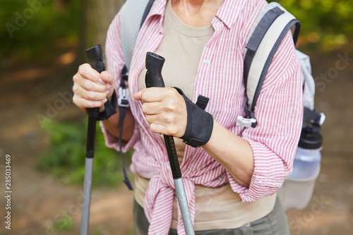 Close-up of mature woman holding canes and doing nordic walking in the forest