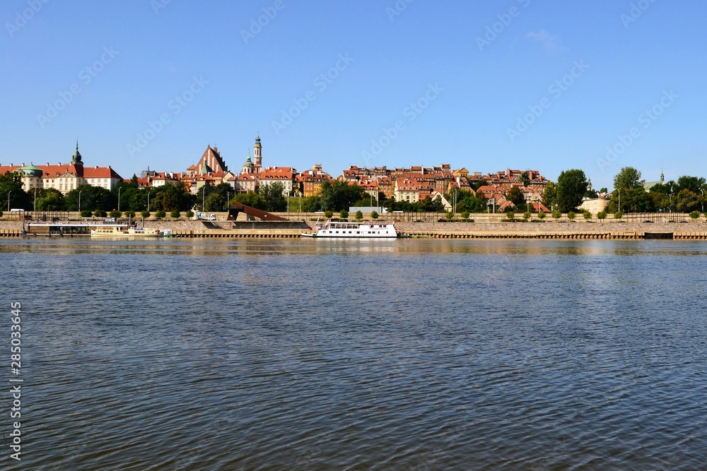 Obraz premium Summer view of the Old Town - historic quarter of Warsaw with Royal Castle and red roof tenements seen from the Vistula river side. Warsaw, Poland