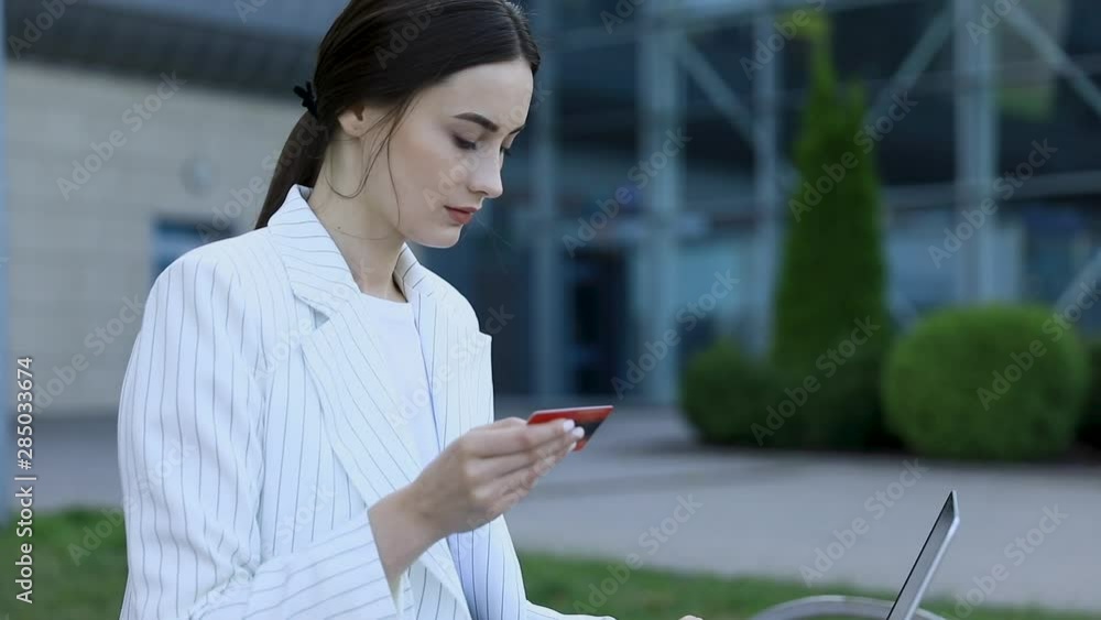 Close-up of young professional businesswoman using her laptop outside while working at modern business center, modern buildings in the background, flare light, film effects, slow motion Close-up of young professional businesswoman using her laptop outside while working at modern business center, modern buildings in the background, flare light, film effects, slow motion