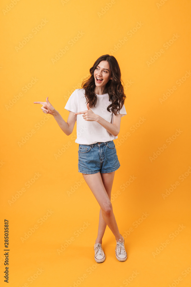 Happy young woman posing isolated over yellow wall background pointing to copyspace. Happy young woman posing isolated over yellow wall background pointing to copyspace.