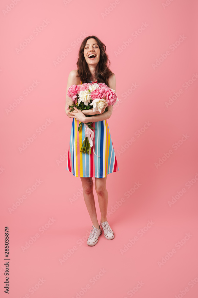 Happy cheery smiling young cute woman posing isolated over pink wall background holding flowers. Happy cheery smiling young cute woman posing isolated over pink wall background holding flowers.