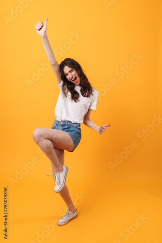 Emotional young woman posing isolated over yellow wall background make winner gesture. © Drobot Dean