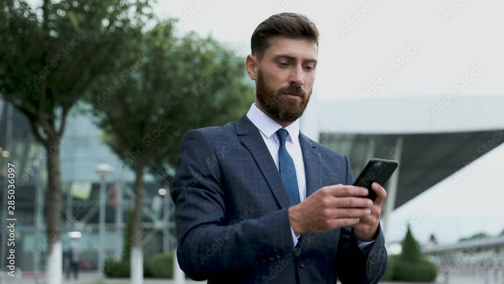 Businessman using smartphone and smiling at airport. Young business executive with mobile phone at airport. Businessman using smartphone and smiling at airport. Young business executive with mobile phone at airport.