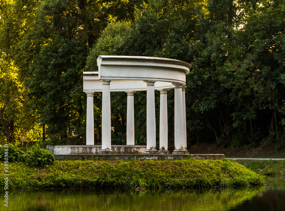 A small building with white columns on the greenery of the park A small building with white columns on the greenery of the park