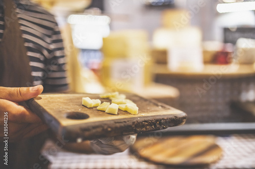 Close up of man holding wooden board with cheese at agricultural fair at street stand.