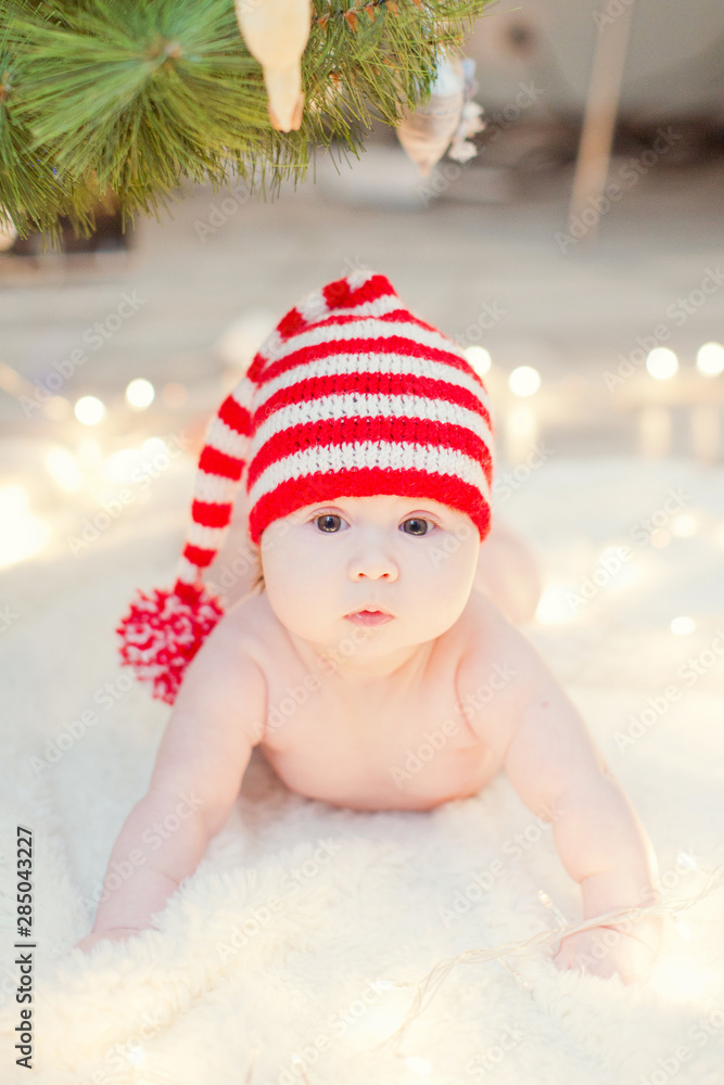 newborn baby in red knit hat near Christmas tree with lights newborn baby in red knit hat near Christmas tree with lights