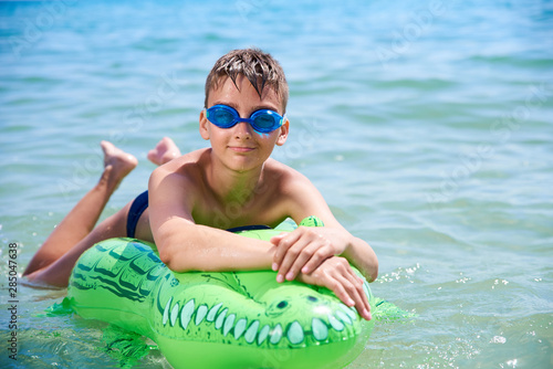 BOY OF TEENAGERS IN WATER GOGGLES SWIMS ON THE INFLATABLE TOY CROCODILE.