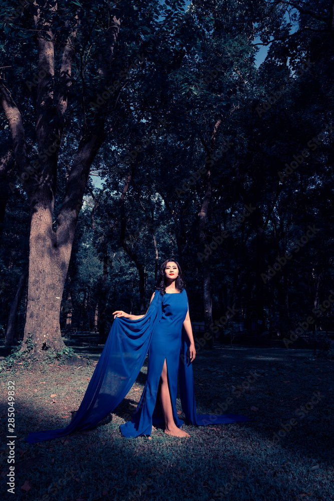 Woman in fashion blue long dress standing under the sunlight in the park Woman in fashion blue long dress standing under the sunlight in the park