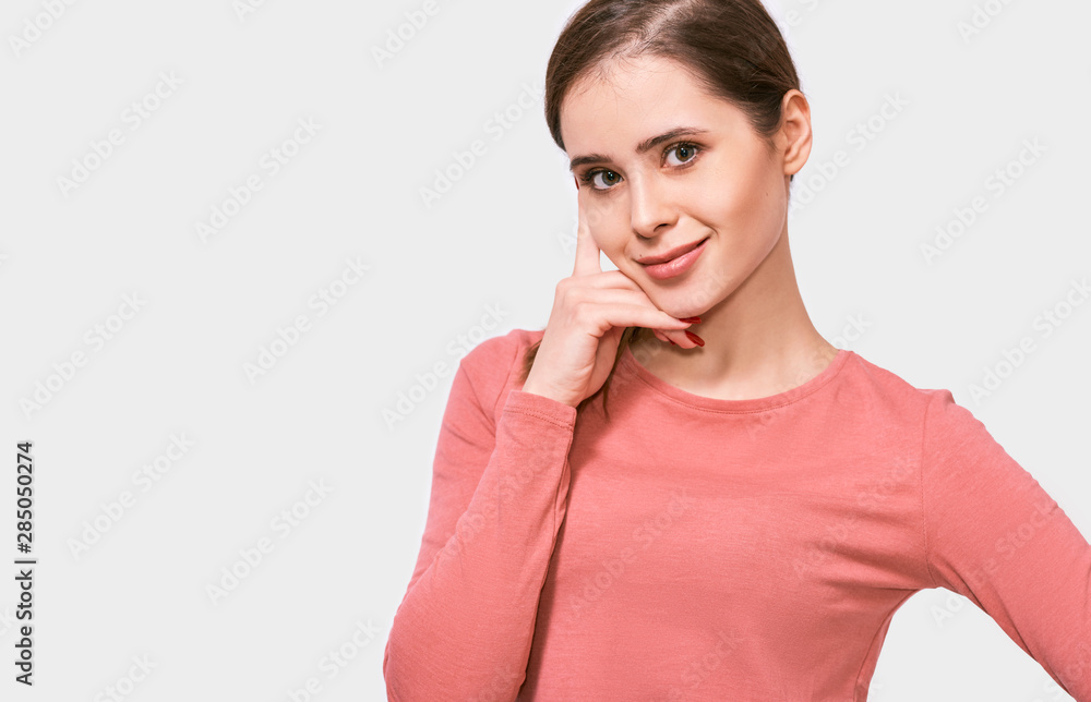 Closeup shot of candid young woman smiling, wearing pink long sleeve shirt, looking to the camera, posing against white background. Pretty female has joyful expression, poses in studio. Closeup shot of candid young woman smiling, wearing pink long sleeve shirt, looking to the camera, posing against white background. Pretty female has joyful expression, poses in studio.