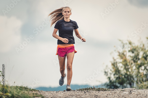 Beautiful blonde athlete runs on dirt road in the hills