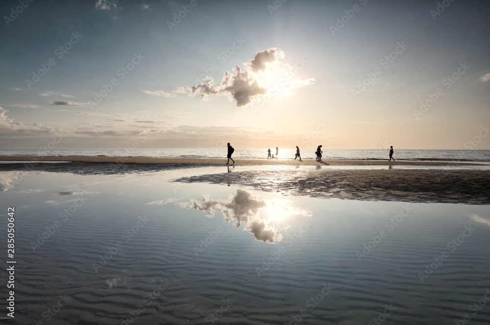 people silhouettes on sea beach against sun