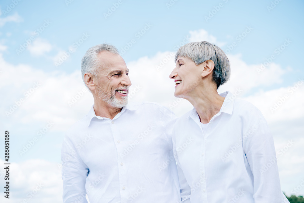 happy smiling senior couple in white shirts looking at each other under blue sky happy smiling senior couple in white shirts looking at each other under blue sky