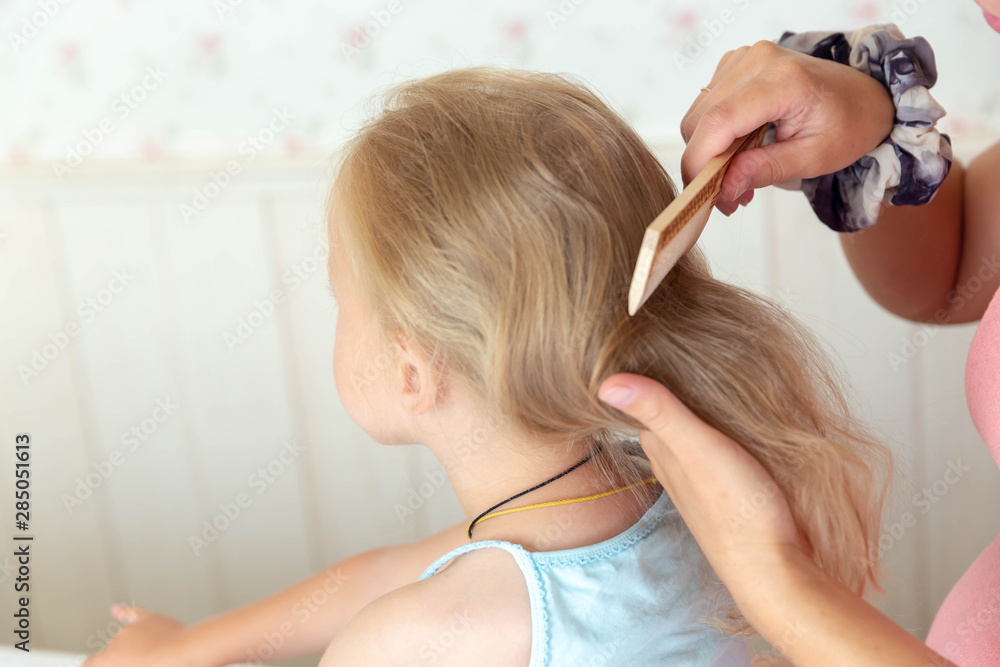 Naklejka premium Women's hands comb the Golden hair of a little girl with a wooden comb.