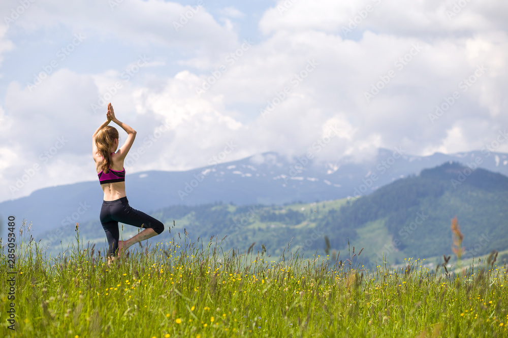 Attractive slim young woman doing yoga exercises outdoors on background of green mountains on sunny summer day. Attractive slim young woman doing yoga exercises outdoors on background of green mountains on sunny summer day.