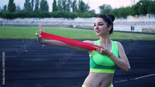 beautiful young girl in a sports green top is engaged with elastic for fitnesss in the stadium photo