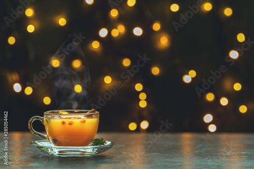 Cup of hot spicy tea with yellow orange barries on dark Christmas and New Year background with light bokeh.