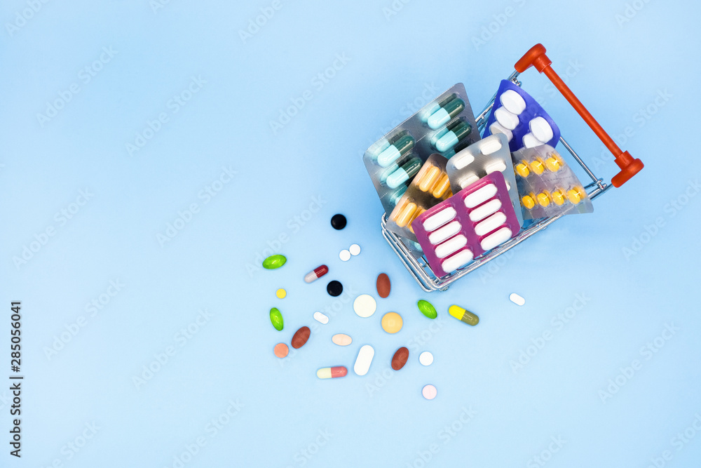 Buy and shopping medicine concept. Capsules, tablets and medicine in shop trolley on a blue background. Creative idea for health care and pharmaceutical company. Copy space., Top view photo.