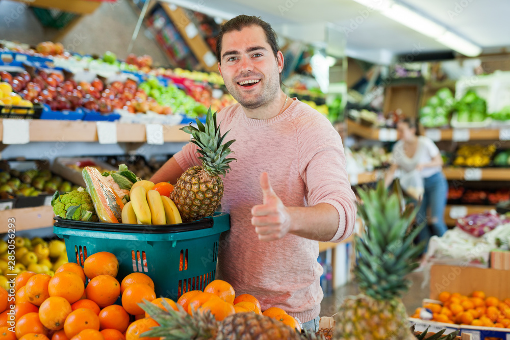 Cheerful man standing with full shopping cart during shopping