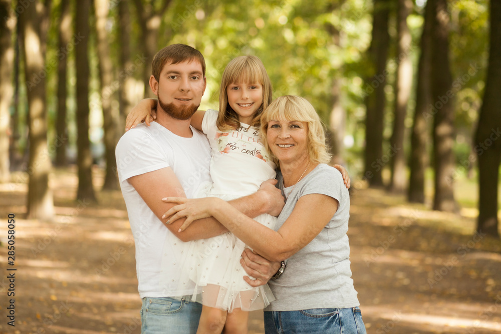 Three generation - grandmother, father, and little daughter. Family and people concept - happy excited smiling family at park outdoors Three generation - grandmother, father, and little daughter. Family and people concept - happy excited smiling family at park outdoors