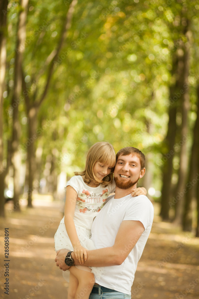 Portrait of lovely smiling daughter in her father's arms walking at green park outside. Happy family people concept Portrait of lovely smiling daughter in her father's arms walking at green park outside. Happy family people concept