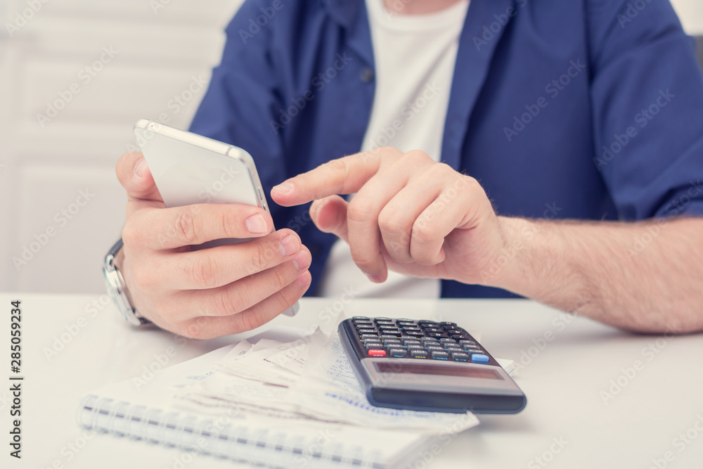 Man calculates family budget, he pays for the expenses with his smartphone, cropped image, men's hands, close up Man calculates family budget, he pays for the expenses with his smartphone, cropped image, men's hands, close up