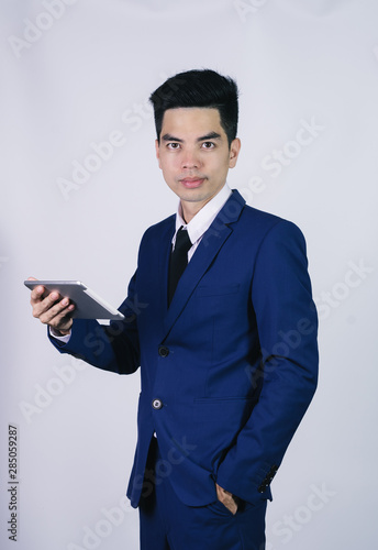 Portrait handsome young asian man wearing a blue suit holding smart phone or tablet smile and happy isolated on gray background in studio. Asian man people. business success concept.