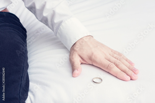 Husband leaves wedding ring in the marital bedroom, sitting on the bed in the home, a man leaves his family to file for divorce, closeup, toned. The concept of divorce and family disintegration