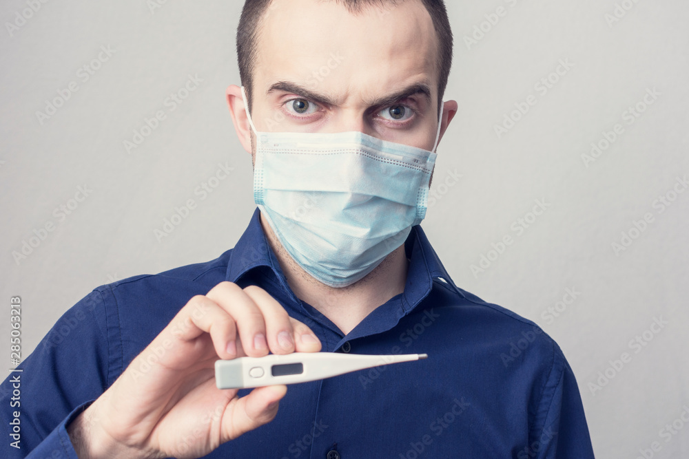 Man in a medical mask show a thermometer in his hand, close up, toned Man in a medical mask show a thermometer in his hand, close up, toned