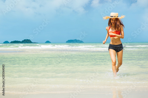 young slim beautiful woman running on beach and blue sky background. woman in bikini and sun hat relaxing at sunny beach.