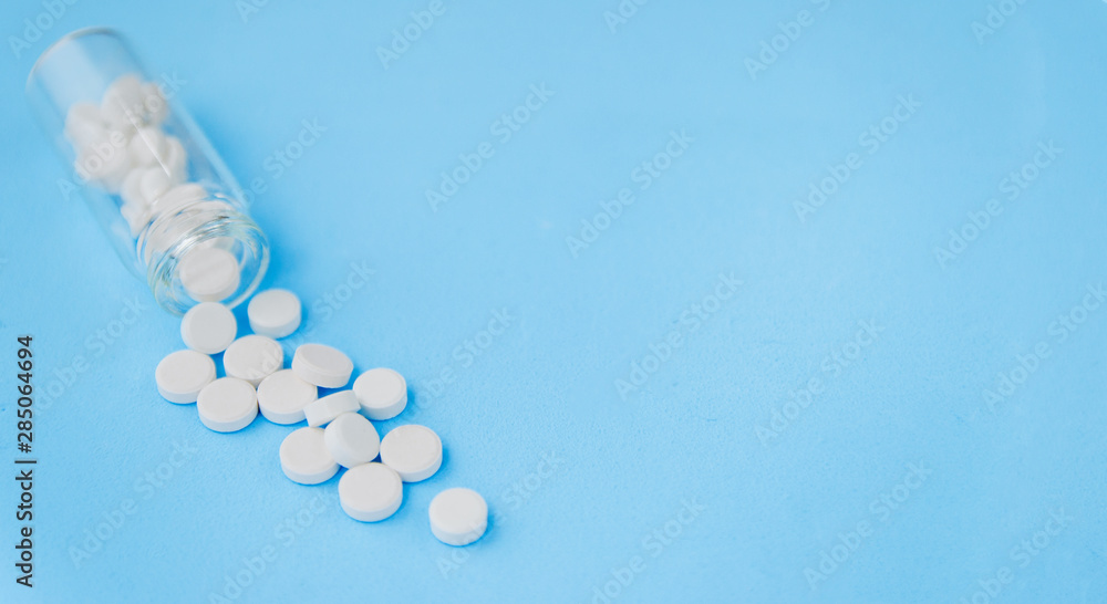 White pills and glass bottle on blue background. Alternative homeopathy is a herb medicine.The concept of health and medicine. Flatley. The view from the top. copyspace for text. White pills and glass bottle on blue background. Alternative homeopathy is a herb medicine.The concept of health and medicine. Flatley. The view from the top. copyspace for text.