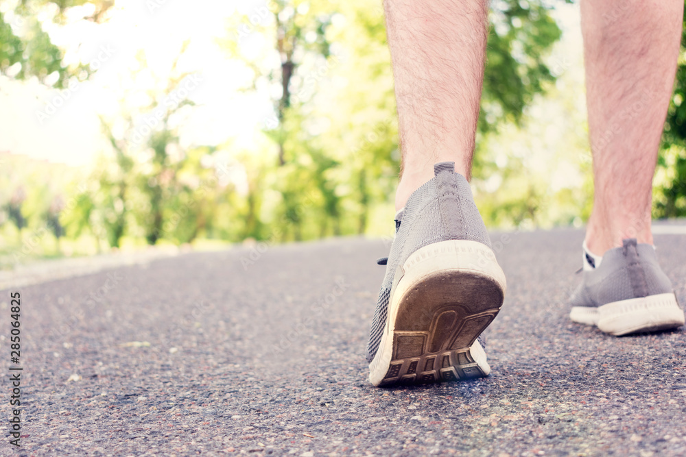 Man walking on the road in the Park in the summer, the man's feet in sneakers, closeup, cropped image, toned. The concept of Hiking Man walking on the road in the Park in the summer, the man's feet in sneakers, closeup, cropped image, toned. The concept of Hiking