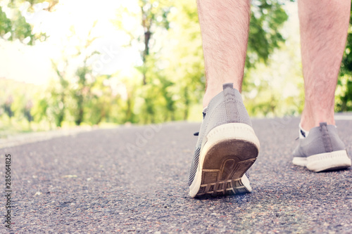 Man walking on the road in the Park in the summer, the man's feet in sneakers, closeup, cropped image, toned. The concept of Hiking