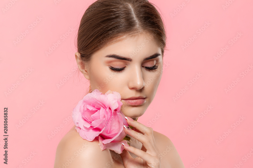 Naklejka premium Close-up portrait of a beautiful young girl with pink rose flower isolated over pink background.