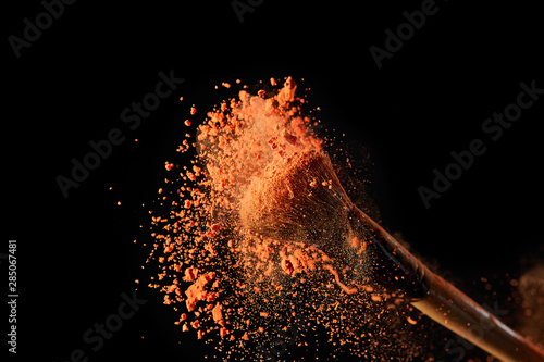 cosmetic brush with bright orange powder explosion on black background
