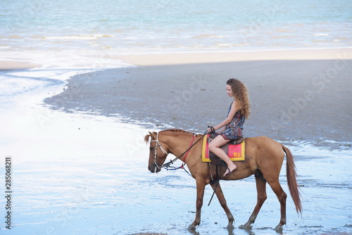 Woman fashion model riding a horse on the beach in summer.