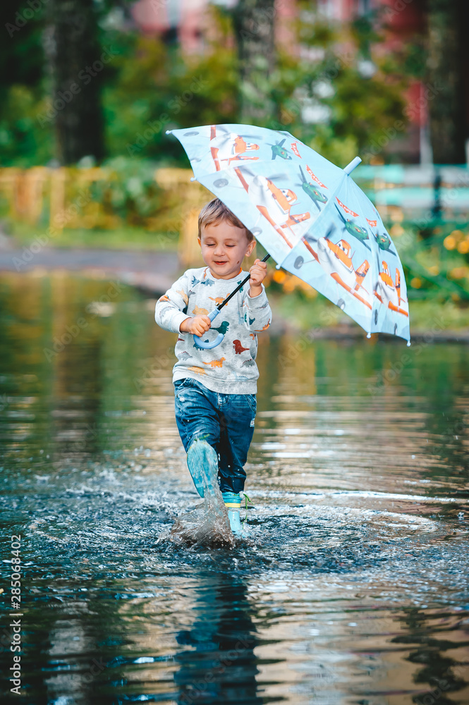 Little boy under colorful umbrella playing in summer park after rain.