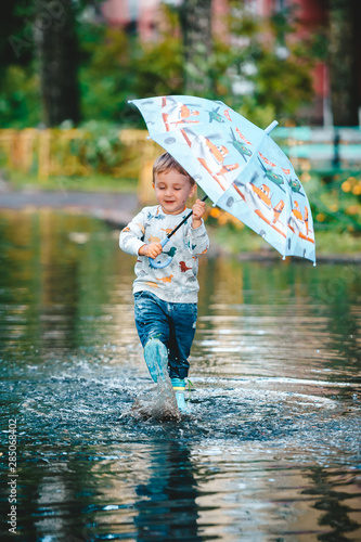 Obraz na płótnie Little boy under colorful umbrella playing in summer park after rain. w salonie