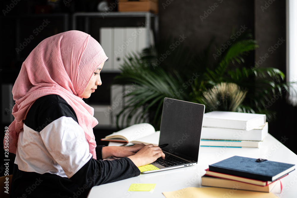 The beautiful muslim woman doing work at home,using laptop for searching data,with interested emotion,blurry light around The beautiful muslim woman doing work at home,using laptop for searching data,with interested emotion,blurry light around