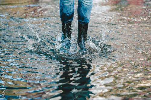 Legs of woman in rubber boots standing in summer puddle