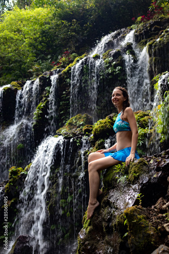 Travel lifestyle. Young traveler woman sitting at waterfall in tropical forest. Banyu Wana Amertha waterfall Wanagiri  Bali  Indonesia.