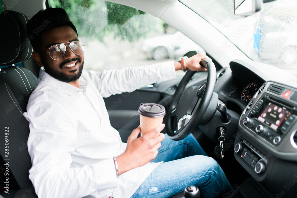 Handsome indian man driving a car with coffee to go