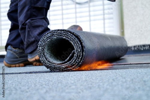 Flat roof installation with propane blowtorch during construction works with roofing felt. Heating and melting bitumen roofing felt. Roofing felt. Roofer working. Roofer working tool. Waterproofing photo