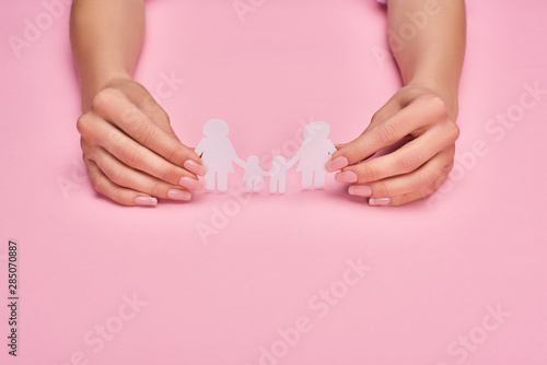 cropped view of woman holding paper cut lesbian family on pink background