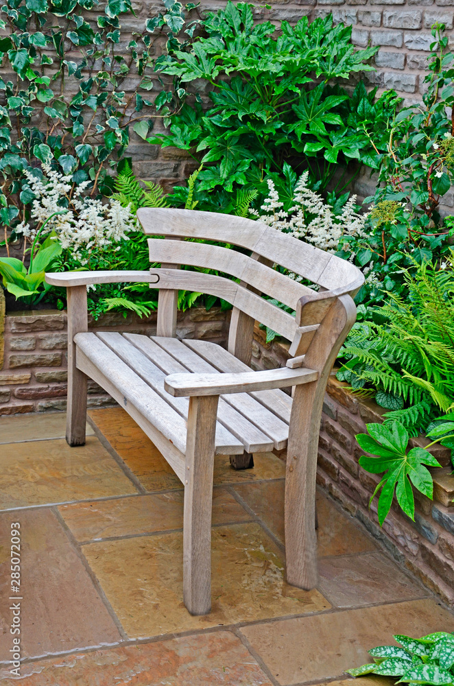 Close up of a wooden garden seat in a walled garden patio with plants