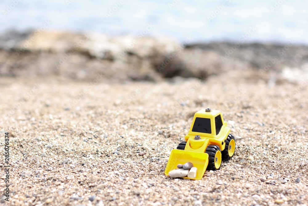 Toy loader on the beach. Excavator rowing sand. Loader loads sand. Children's toys for sand. Yellow excavator toy in the sand, on the beach. Summer holiday or summer vacation concept. Toy loader on the beach. Excavator rowing sand. Loader loads sand. Children's toys for sand. Yellow excavator toy in the sand, on the beach. Summer holiday or summer vacation concept.