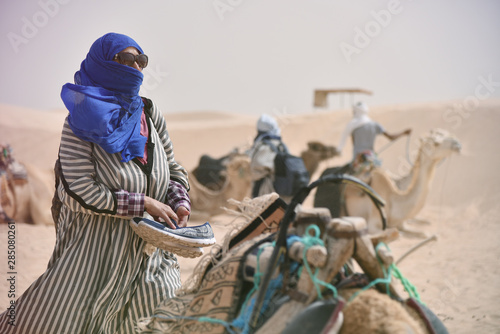 Female middle age tourist in traditional clothes riding camel in sahara desert, Tunis. Middle age woman in traditional cloth riding the camel.