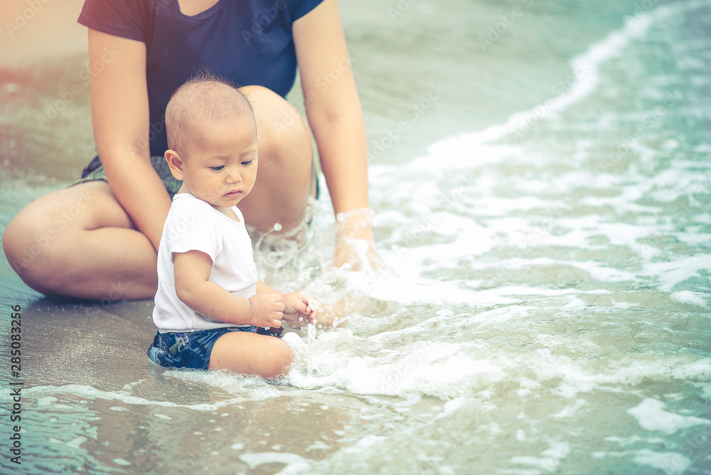 Little Asian 10 months baby excited playing the beach first time. Mother closely take care baby while playing the water. Little Asian 10 months baby excited playing the beach first time. Mother closely take care baby while playing the water.