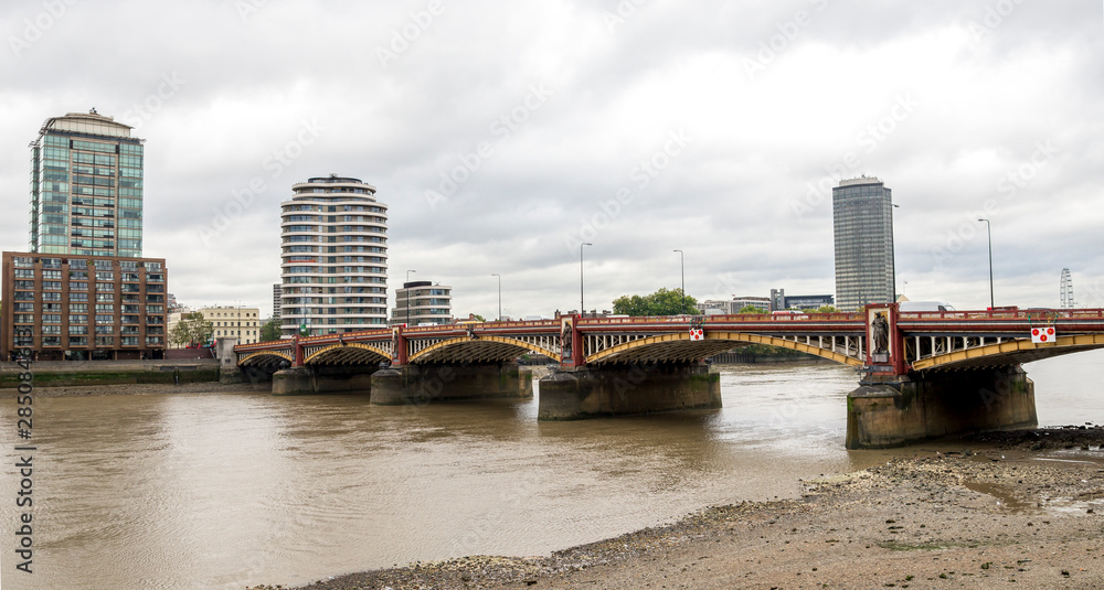 Vauxhall traffic and footbridge and dirty shore of river Thames, London, England