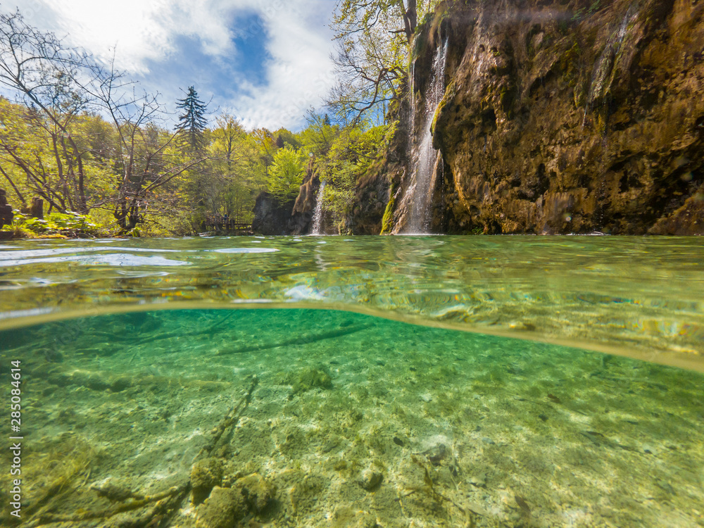 Amazing split view of lake with sunken tree trunk and waterfall in the background. Plitvice national park, Croatia.